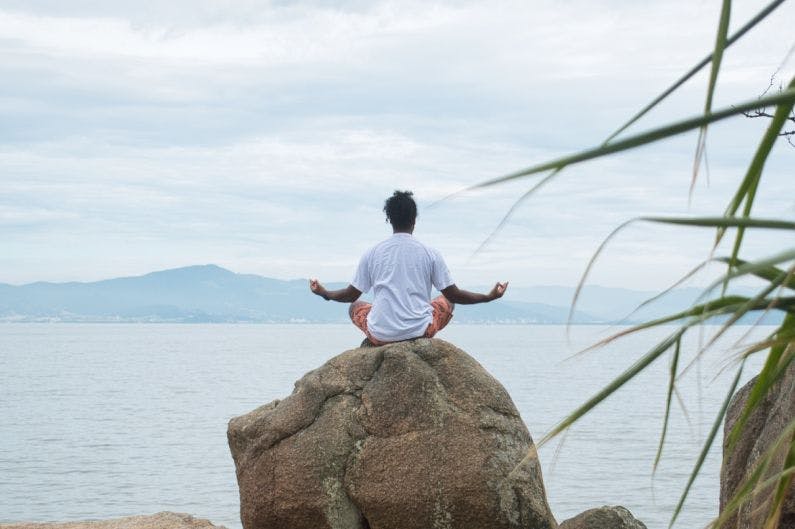 Pierre in a lotus position on top of a rock with sea in front of him